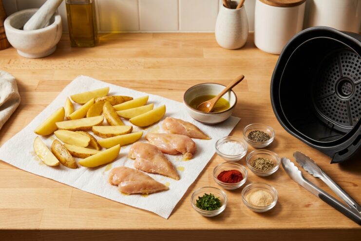 Raw chicken, potatoes, and spices prepared for cooking in an air fryer