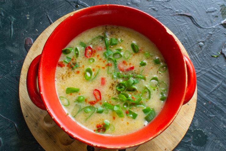 Creamy cheese soup garnished with fresh chili and green onions in a bright red bowl