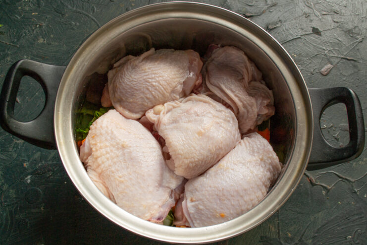 Adding chicken to the pot Raw chicken thighs placed on top of vegetables in a pot