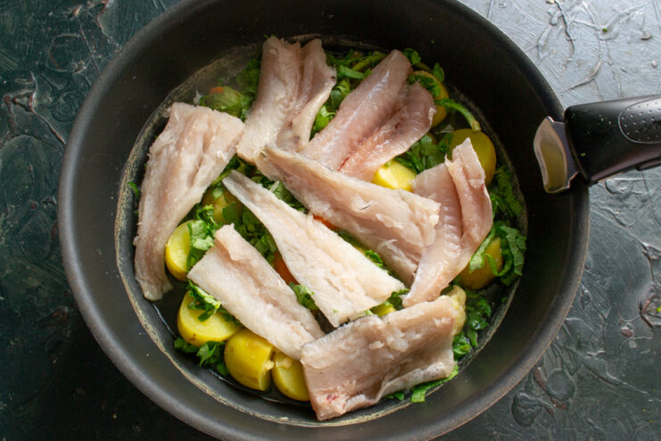 Layering the fish Raw chunks of white fish fillet layered over cooked spinach inside a pot