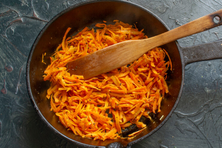 Braising carrots for pate Grated carrots seasoned with dried parsley cooking in a skillet with a wooden spatula
