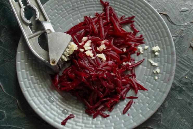 Grating beet and pressing garlic Finely grated beet and minced garlic prepared on a gray plate.