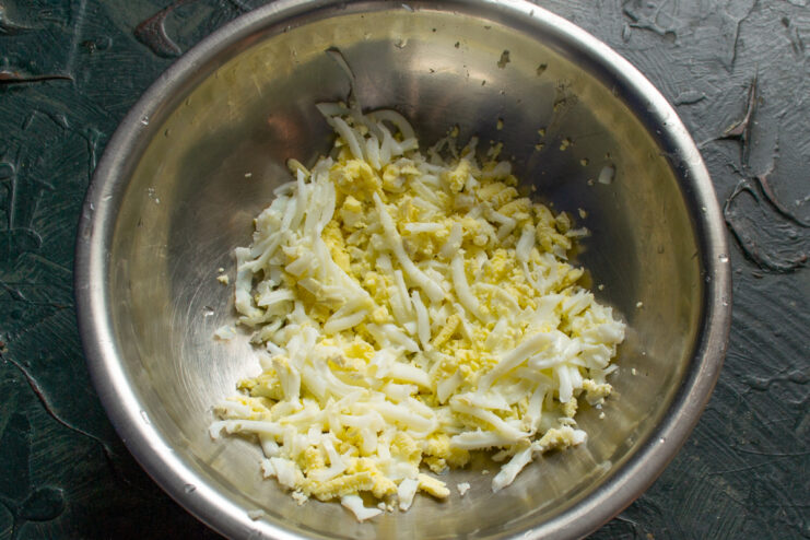 Grating the boiled eggs Grated hard-boiled eggs in a metal mixing bowl
