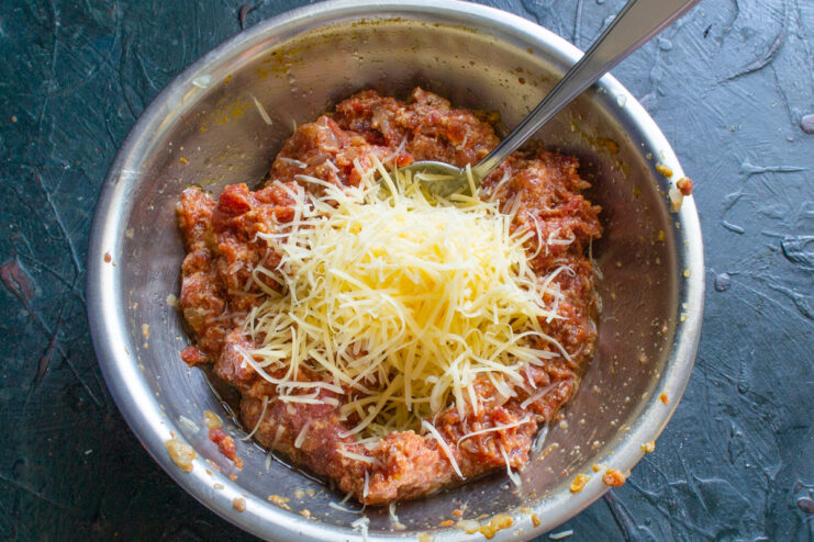 Folding In The Cheese Grated hard cheese being added to the prepared meat mixture
