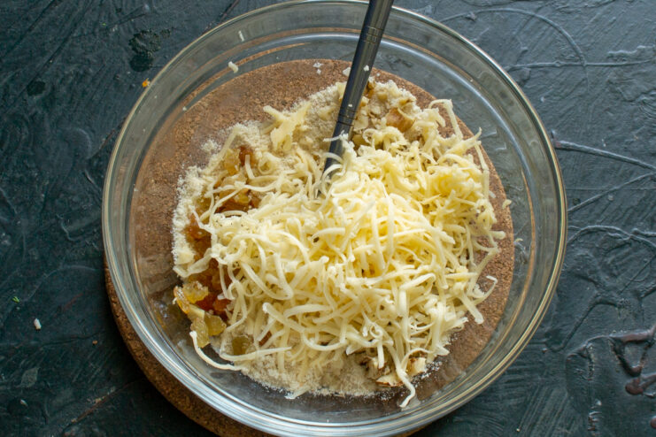 Adding grated hard cheese to the mixture Grated hard cheese sprinkled into the bowl with the walnut and raisin filling mixture.