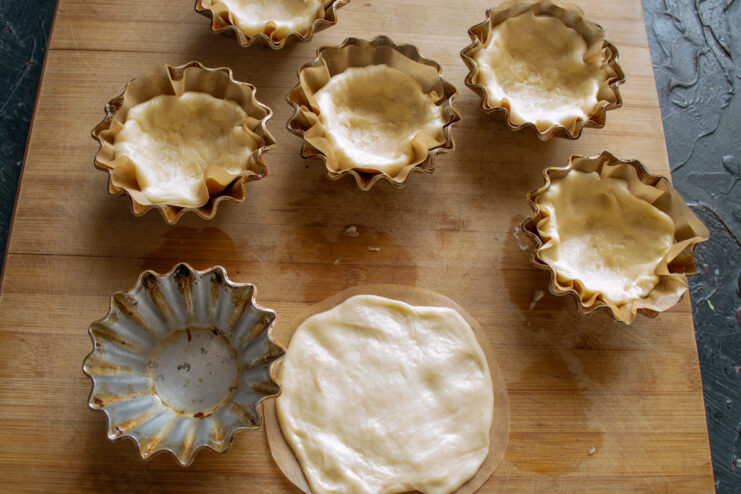 Preparing Baking Shells Pastry dough being pressed and shaped into metal muffin tins
