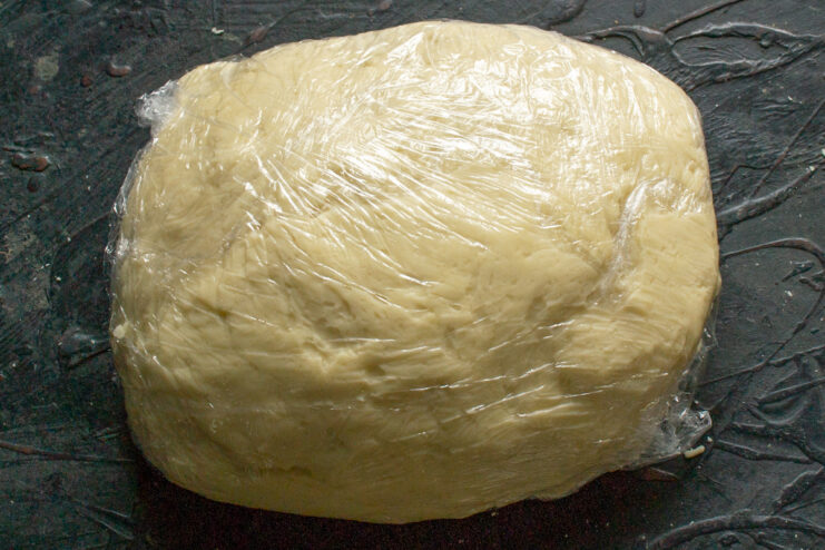Dough wrapped tightly in plastic wrap resting on a table