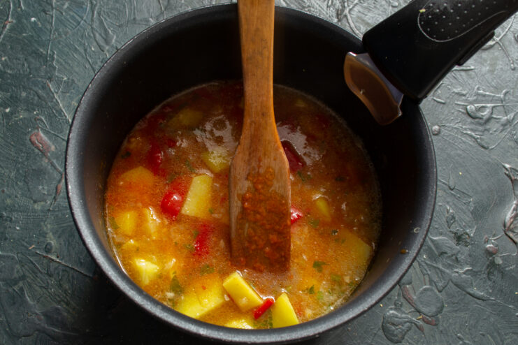Smooth tomato puree being mixed into simmering vegetables and fish broth.