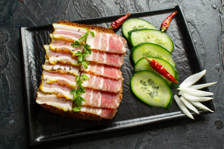 Serving the Cured Pork Belly Thin slices of homemade cured pork belly served with fresh vegetables on a plate
