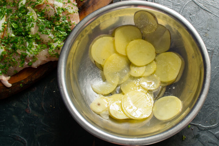Very thin raw potato slices tossed in oil in a glass bowl