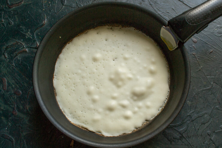 Pouring batter into a hot skillet Pouring and spreading thin crepe batter onto a hot frying pan