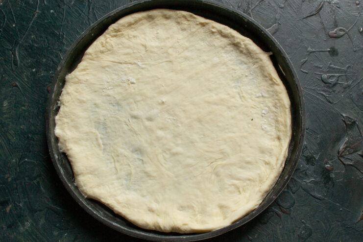 Pizza base in the baking pan Thin pizza dough placed on a round metal baking sheet