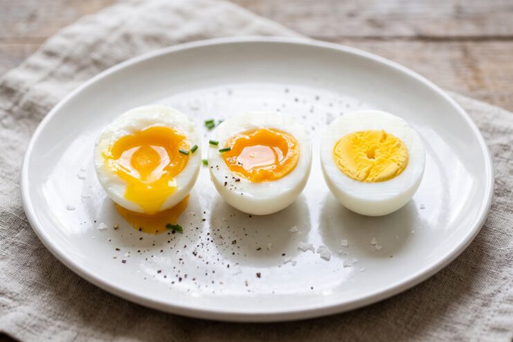 Three Stages of Boiled Eggs Three boiled eggs sliced in half on a plate showing soft, medium, and hard-boiled yolks.