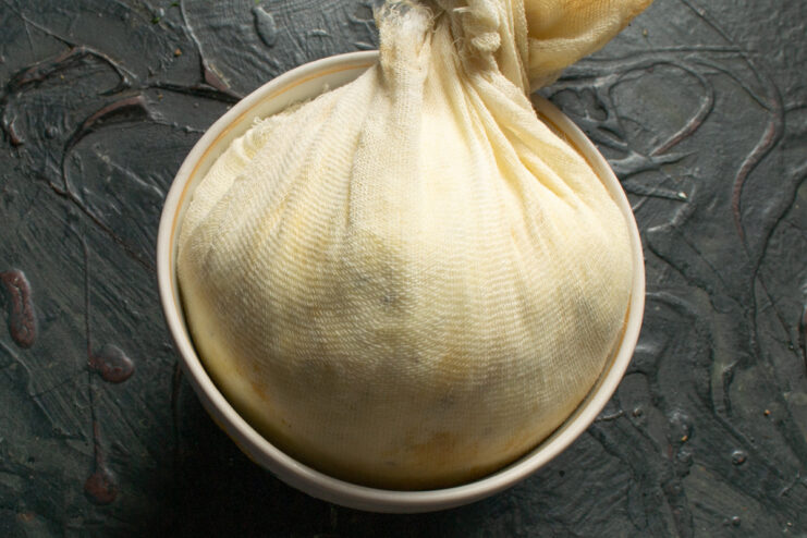 Wrapped cheese before chilling Cheese tightly bound in a cheesecloth bundle inside a bowl