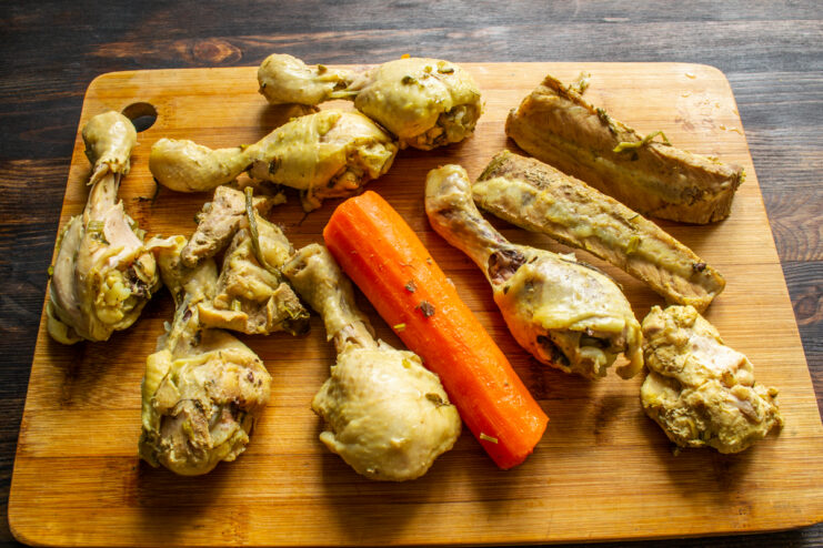 Cooling The Cooked Meat Boiled chicken drumsticks, ribs, and carrot on a board