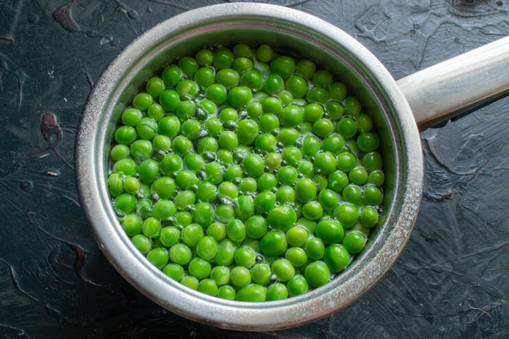 Boiling fresh green peas in a pot of hot brine on a stove