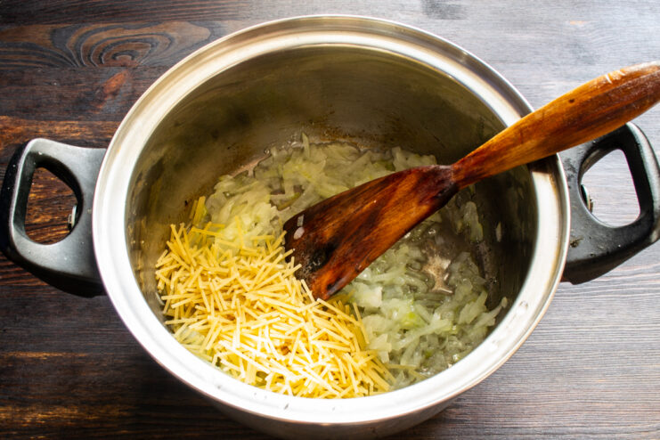 Dry vermicelli added to sautéed onions in a pot