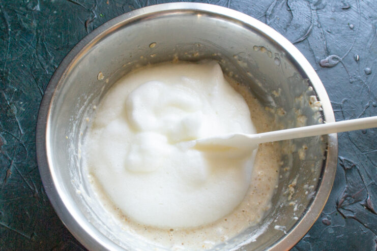 Adding the egg white Whipped egg white placed on top of the oat batter in a bowl