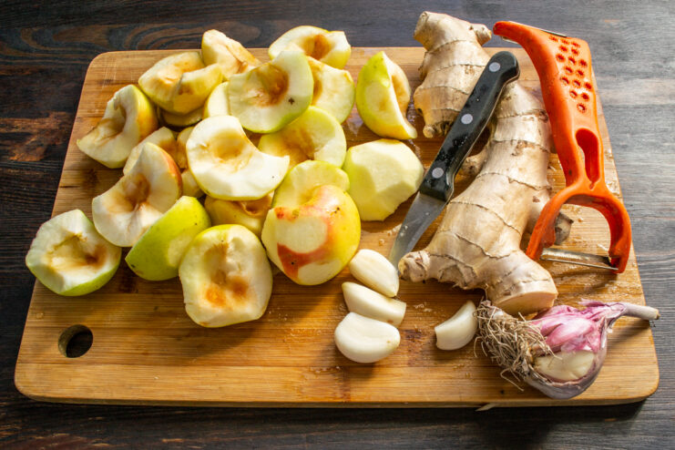 Prepping Key Ingredients Fresh apples, peeled ginger root, and whole garlic cloves resting on a cutting board