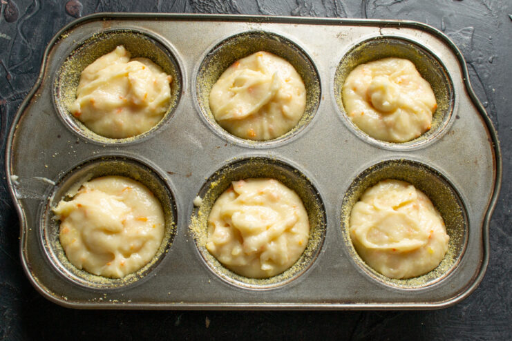 Filling the muffin cups Distributing the rested muffin batter equally into the cups of the tin