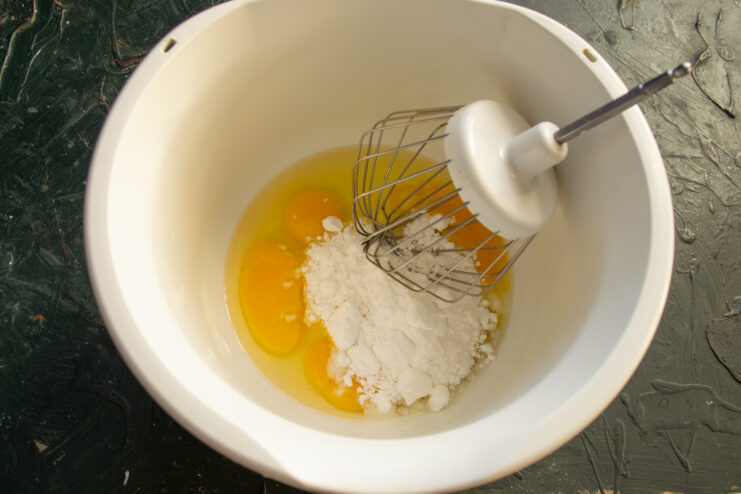 Preparing The Egg Mixture Eggs and powdered sugar in a glass mixing bowl