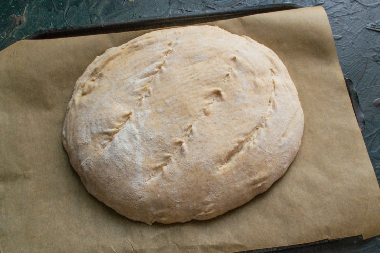 Scoring The Dough Scored bread dough resting on parchment paper before going into the oven.