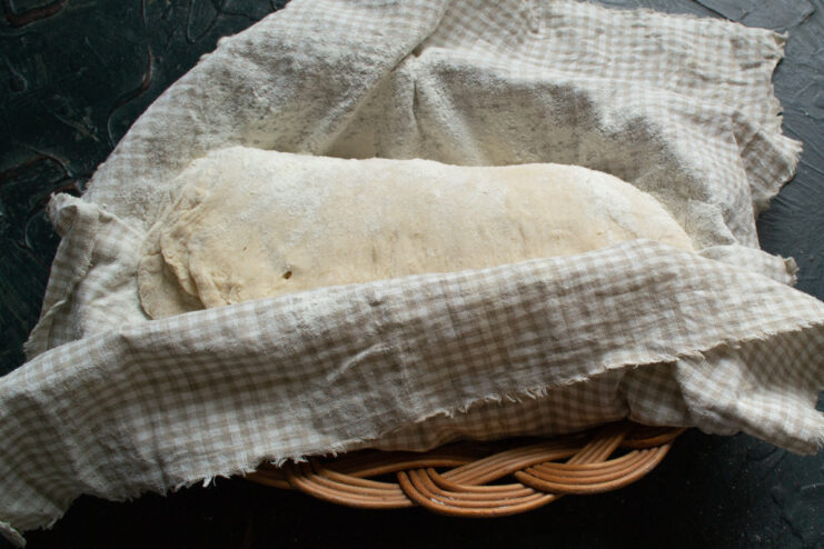 Placing shaped loaf in basket Shaped dough placed seam-side up in a flour-dusted cloth-lined proofing basket