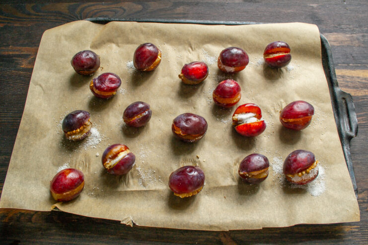 Fully closed stuffed plums arranged on a baking tray before entering the oven