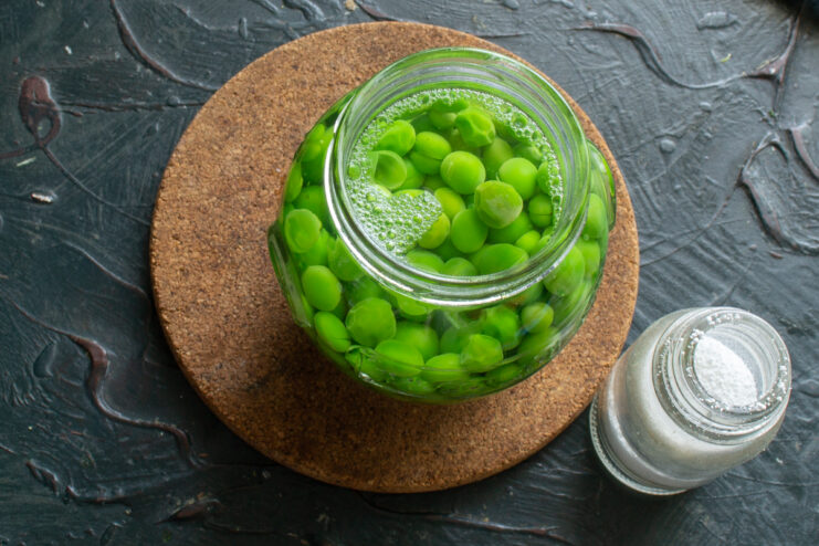 Pouring hot liquid brine over green peas in a glass jar