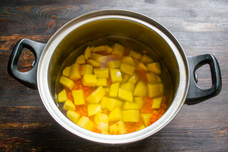 Pouring broth into the soup Pouring hot water over potatoes and lentils in a pot