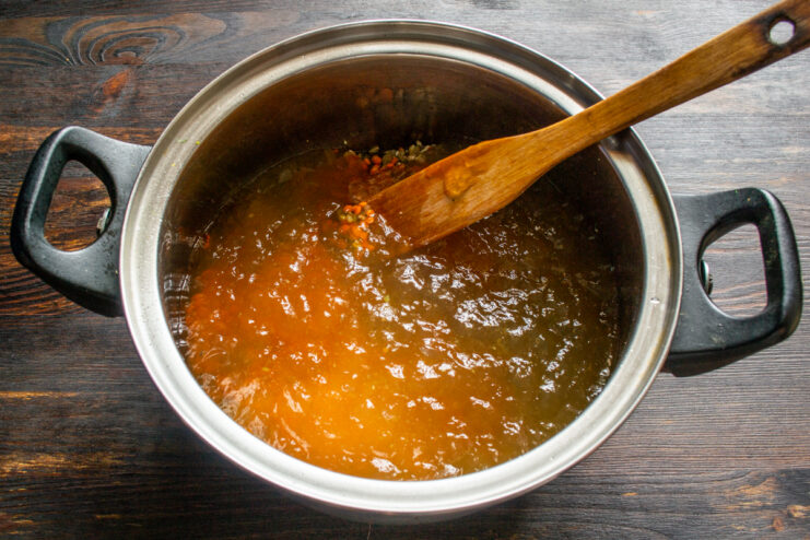 Pouring rich chicken broth into the pot with grains and legumes