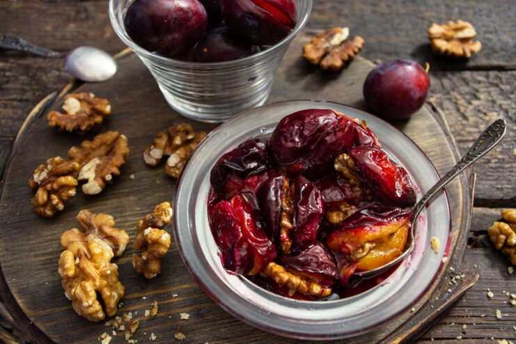 Baked plums stuffed with walnuts served in a glass bowl on a rustic wooden background