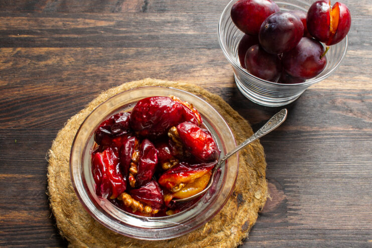 Tender baked plums swimming in natural syrup inside a small glass serving dish