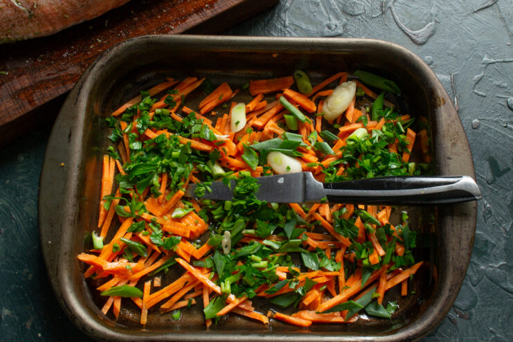 Adding Fresh Herbs Chopped green onions and parsley mixed with carrots in a baking dish