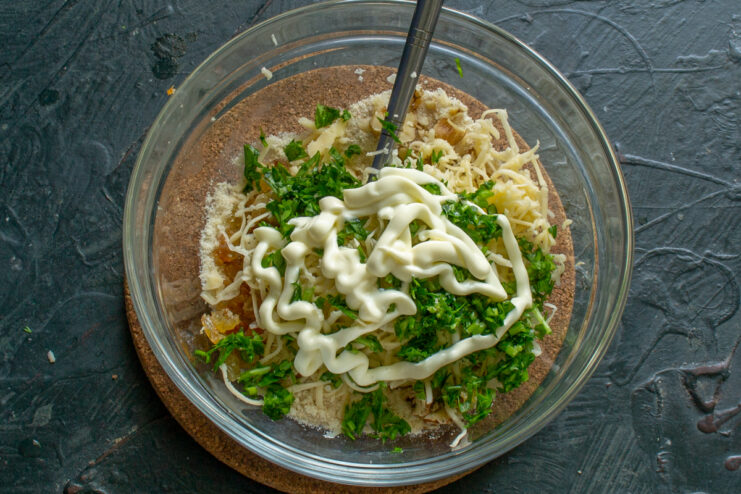 Binding the filling with parsley and mayonnaise Fresh chopped parsley and mayonnaise added to the bowl to bind the filling ingredients.
