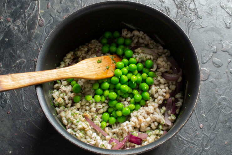 Adding the peas Mixing bright green peas into the pearl barley in a pan