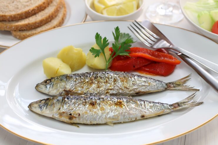 Freshly grilled sardines served on a plate alongside boiled potatoes and roasted bell peppers