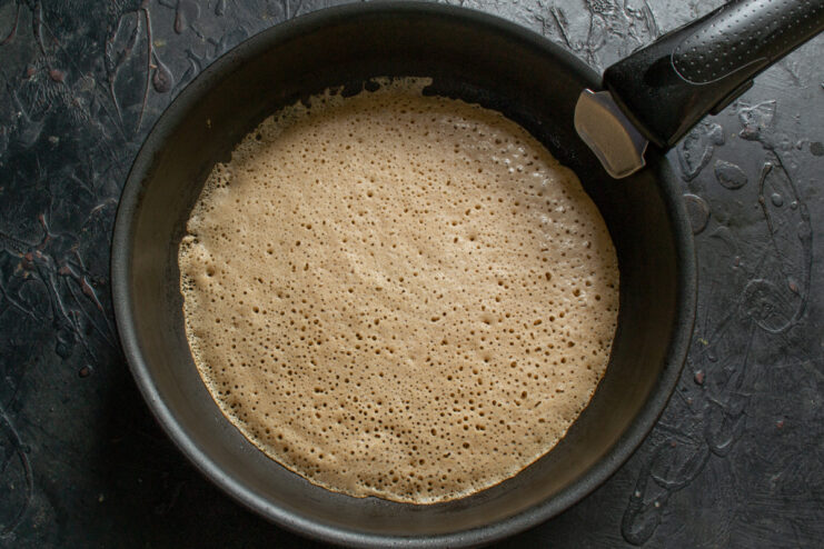 Cooking the chocolate crepe on a skillet Cooking a chocolate crepe in a skillet until small holes appear