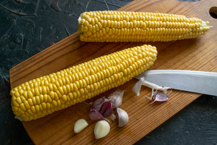Garlic for baking corn Fresh garlic cloves and a corn cob on a cutting board