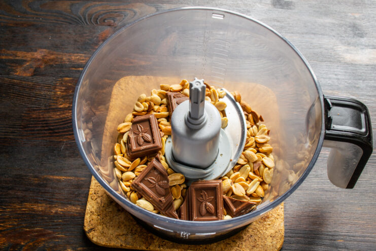 Milk chocolate pieces mixed with warm peanuts in a blender bowl.