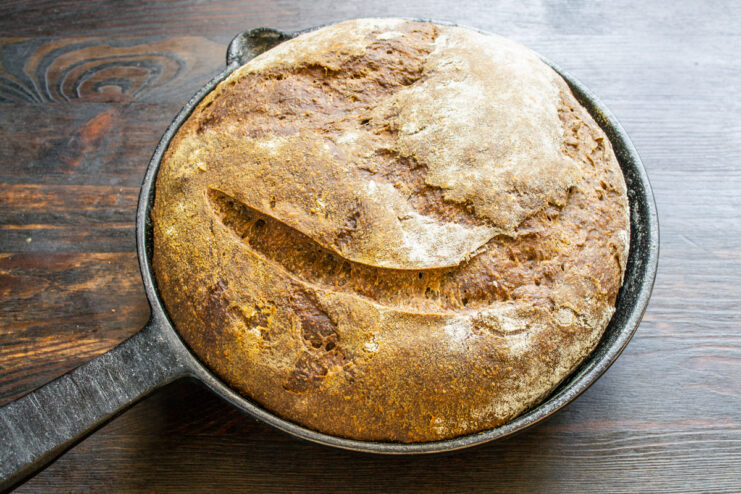 Whole baked rye bread with a score mark in a cast-iron skillet
