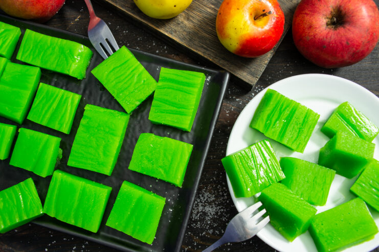 Vibrant green homemade apple marmalade squares plated alongside fresh apples.