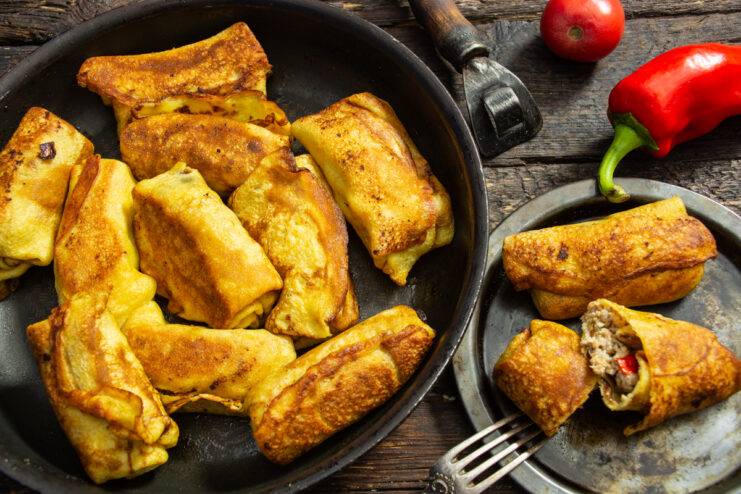 Golden pan-fried stuffed crepes with meat and bell peppers in a skillet