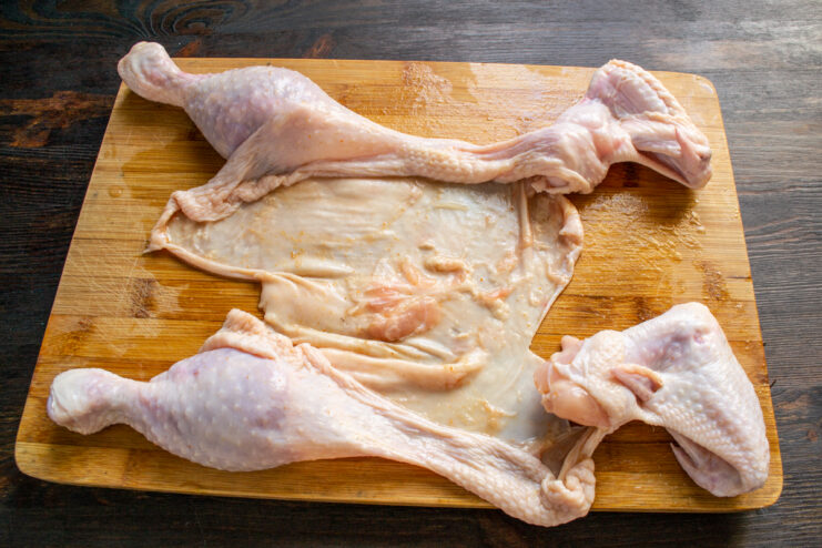 Raw chicken skin laid out flat on a wooden cutting board.