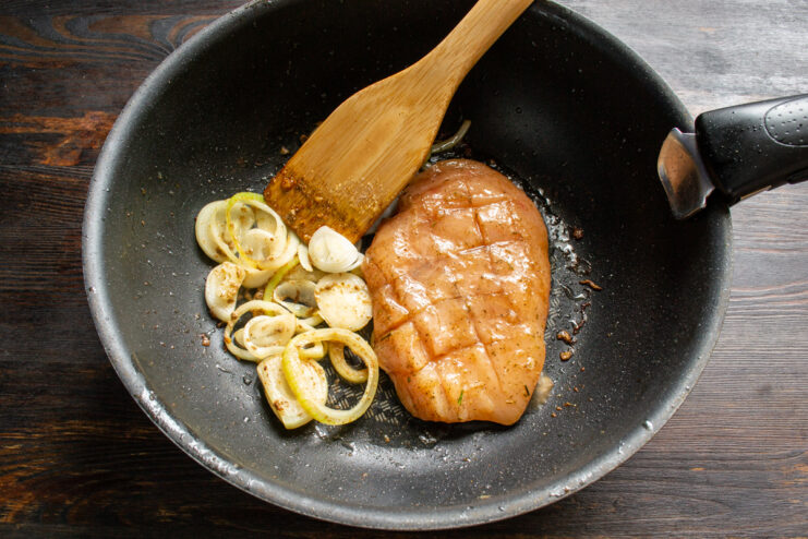 Pan-frying the chicken Chicken breast searing in a pan next to sautéed onions