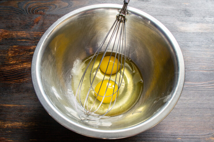 Preparing The Batter Base Chicken eggs, salt, and sugar in a metal mixing bowl with a whisk