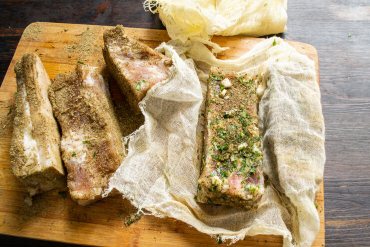 Spiced pork belly cuts wrapped in cheesecloth resting on a wooden board
