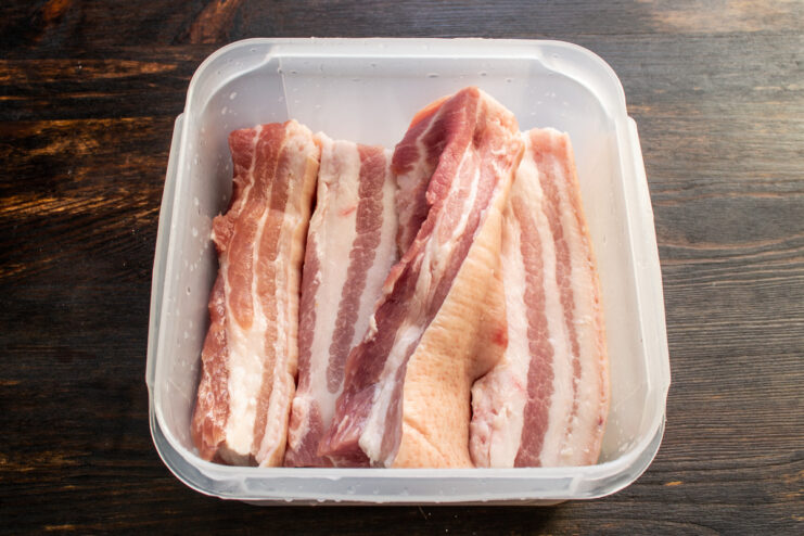 Raw pork belly strips neatly packed into a plastic food container