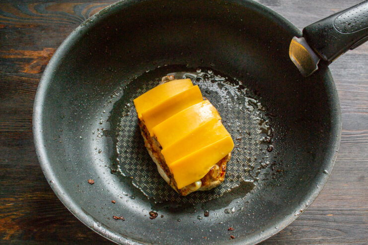 Adding Cheddar cheese Slices of Cheddar cheese layered over a chicken breast and onions