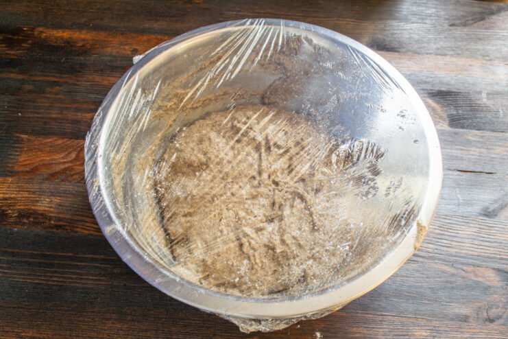 Metal bowl with rye dough tightly covered in plastic wrap